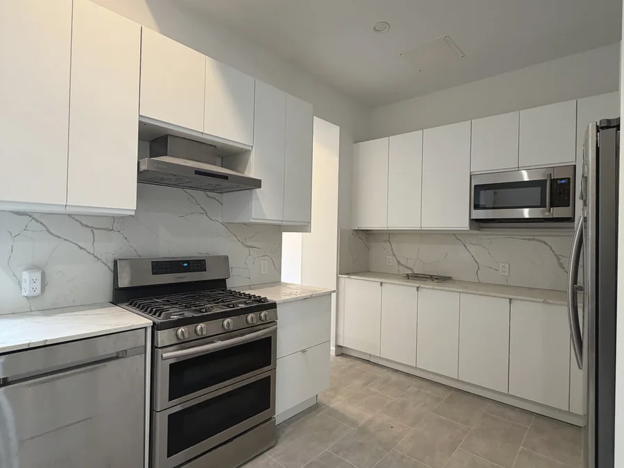 Finished NYC kitchen renovation with white cabinets, stone backsplash, tile floor, and stainless appliances